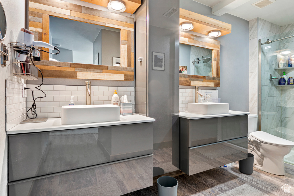 Bathroom with toilet, vanity, tiled shower, decorative backsplash, and hardwood / wood-style flooring