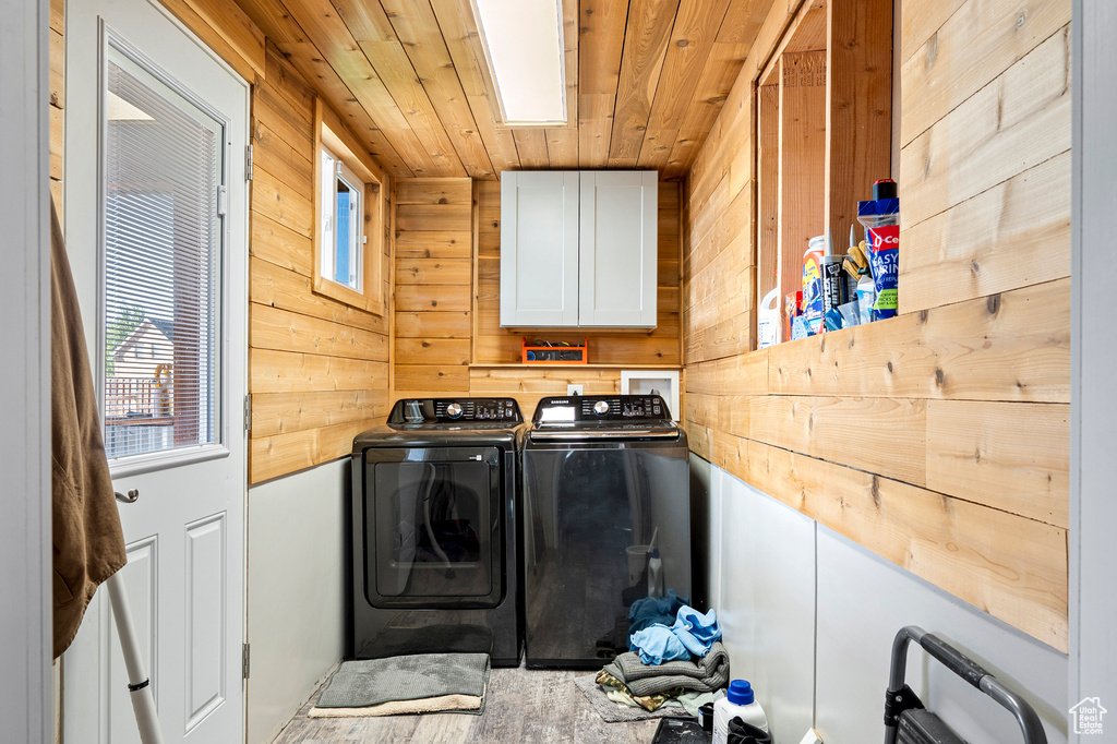 Washroom featuring wood walls, wooden ceiling, cabinets, washer and clothes dryer, and a skylight