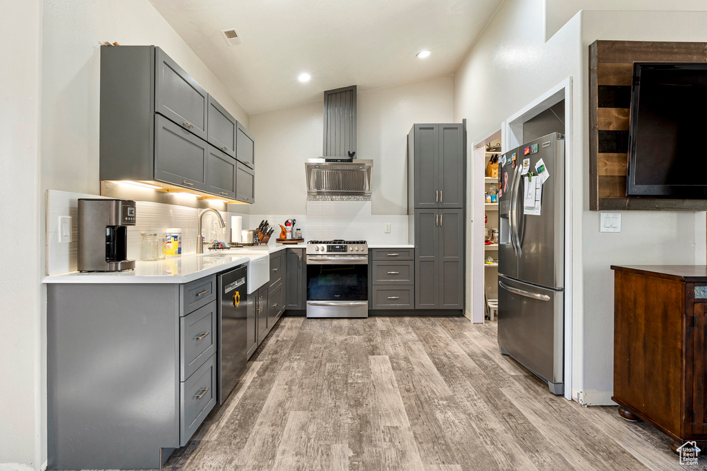 Kitchen with gray cabinets, light hardwood / wood-style flooring, backsplash, appliances with stainless steel finishes, and lofted ceiling