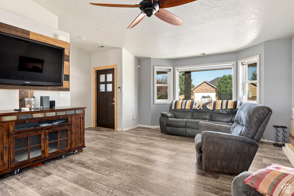 Living room with a textured ceiling, light hardwood / wood-style flooring, and ceiling fan