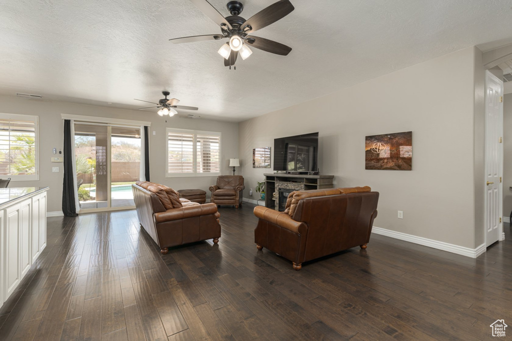 Living room featuring a healthy amount of sunlight, a stone fireplace, ceiling fan, and dark hardwood / wood-style floors