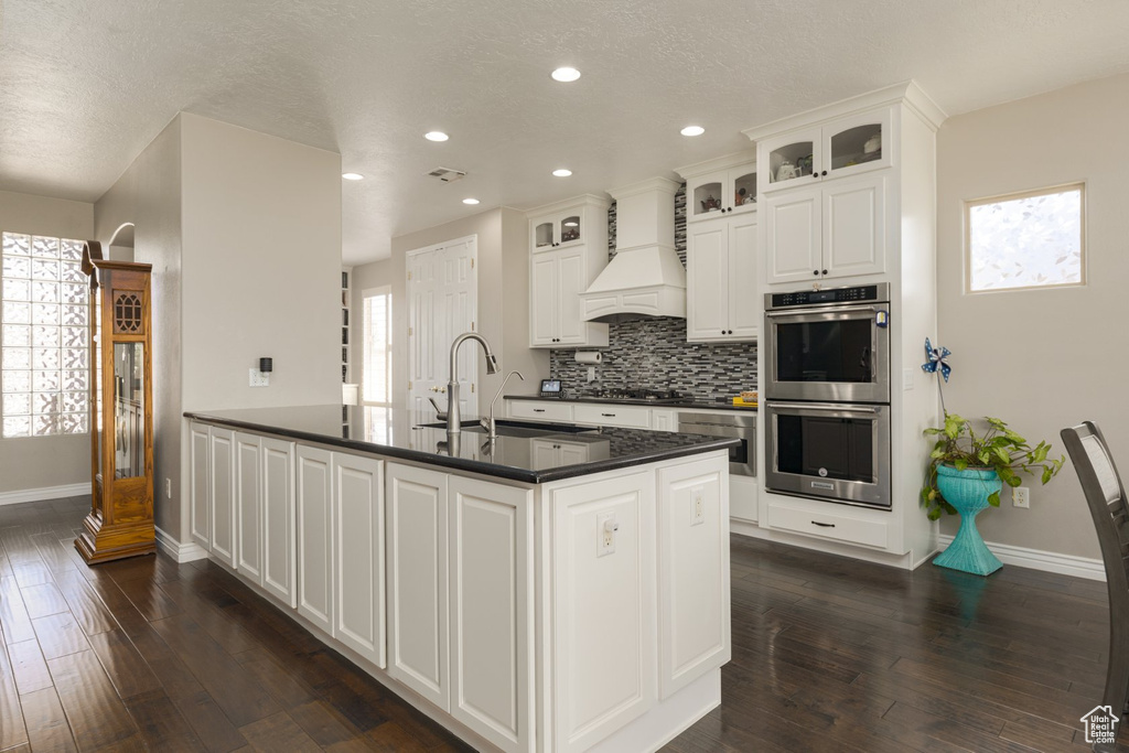 Kitchen featuring white cabinetry, stainless steel double oven, premium range hood, and dark hardwood / wood-style flooring