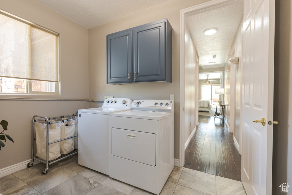 Clothes washing area featuring light wood-type flooring, a healthy amount of sunlight, cabinets, and washing machine and clothes dryer