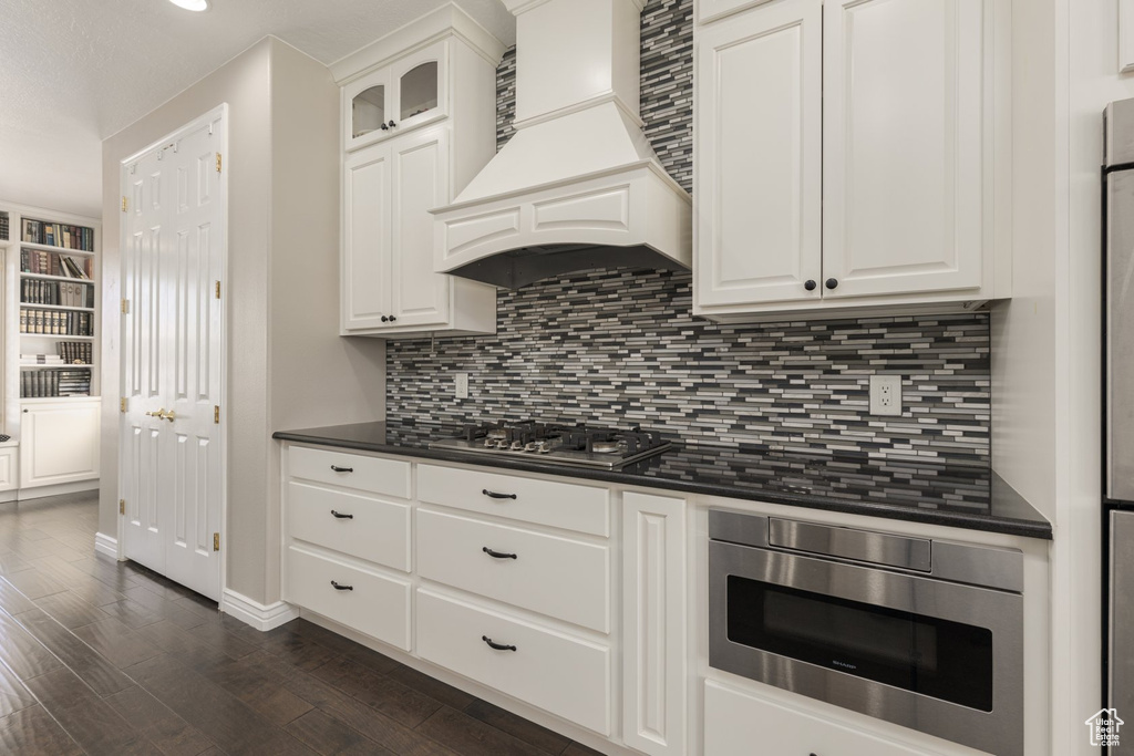 Kitchen with white cabinetry, appliances with stainless steel finishes, dark hardwood / wood-style flooring, and premium range hood