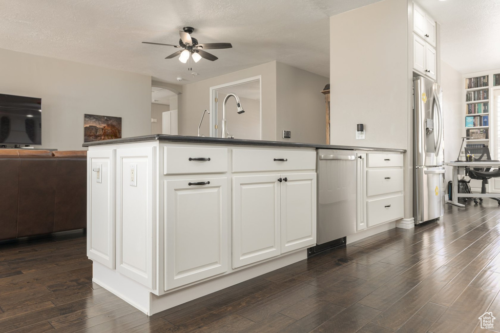 Kitchen with a textured ceiling, appliances with stainless steel finishes, dark wood-type flooring, ceiling fan, and white cabinets