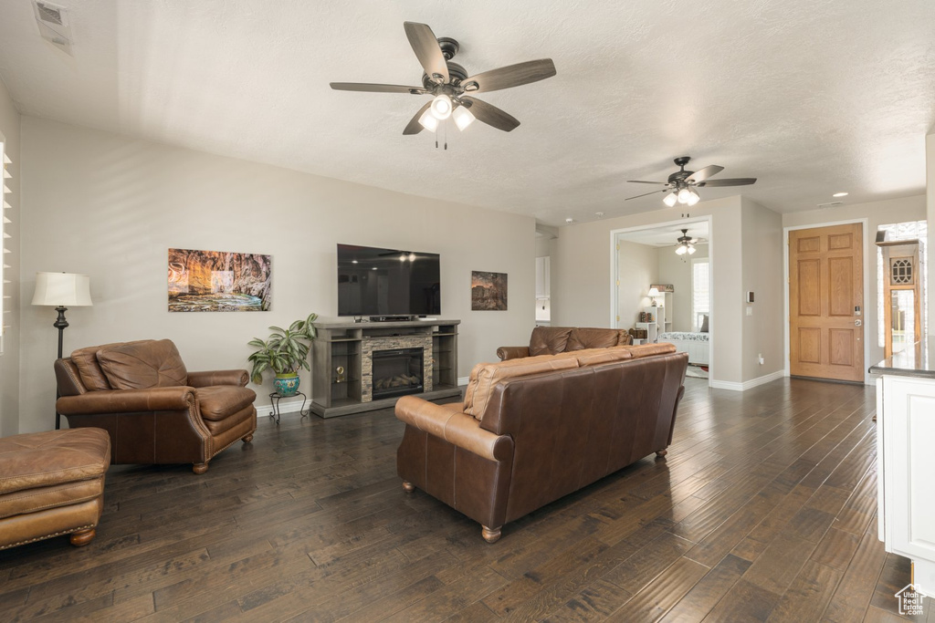 Living room featuring ceiling fan, a stone fireplace, and dark hardwood / wood-style flooring