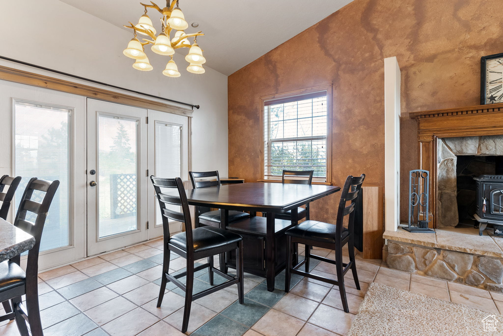 Tiled dining space featuring lofted ceiling, a wood stove, and a notable chandelier