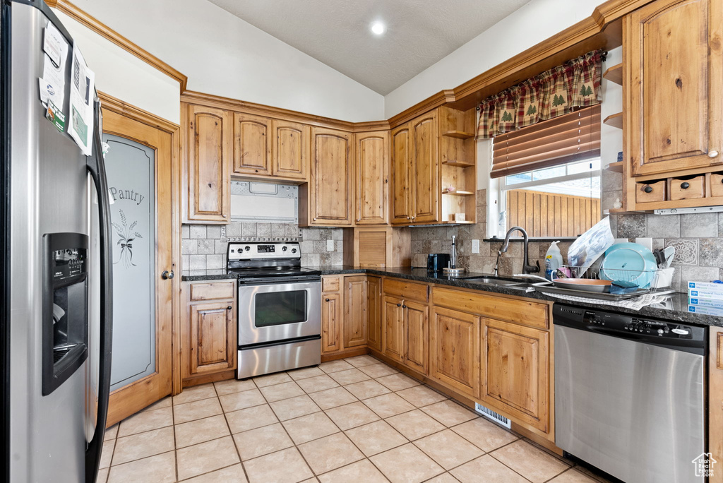 Kitchen with vaulted ceiling, sink, stainless steel appliances, and dark stone counters