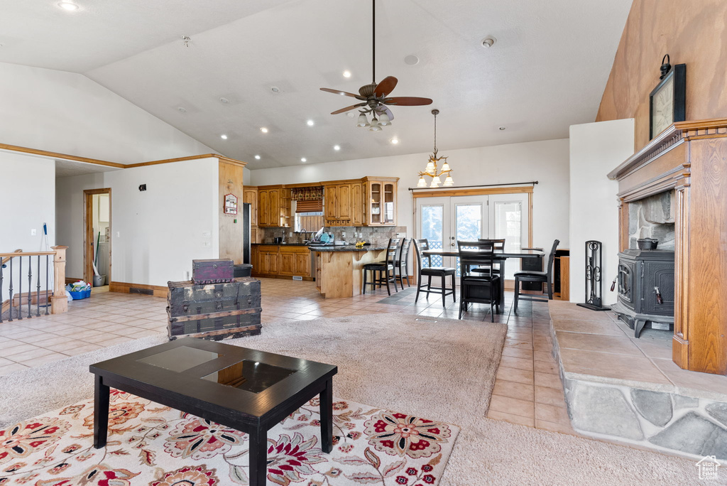 Carpeted living room with ceiling fan with notable chandelier, french doors, high vaulted ceiling, and a wood stove