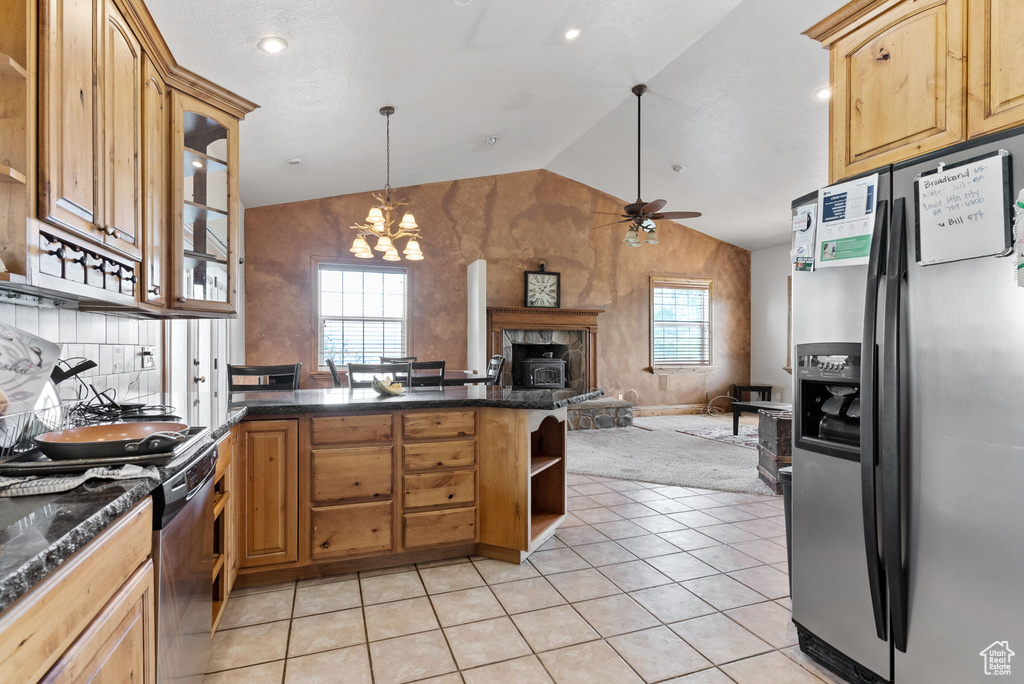 Kitchen with ceiling fan with notable chandelier, a wealth of natural light, vaulted ceiling, a stone fireplace, and appliances with stainless steel finishes