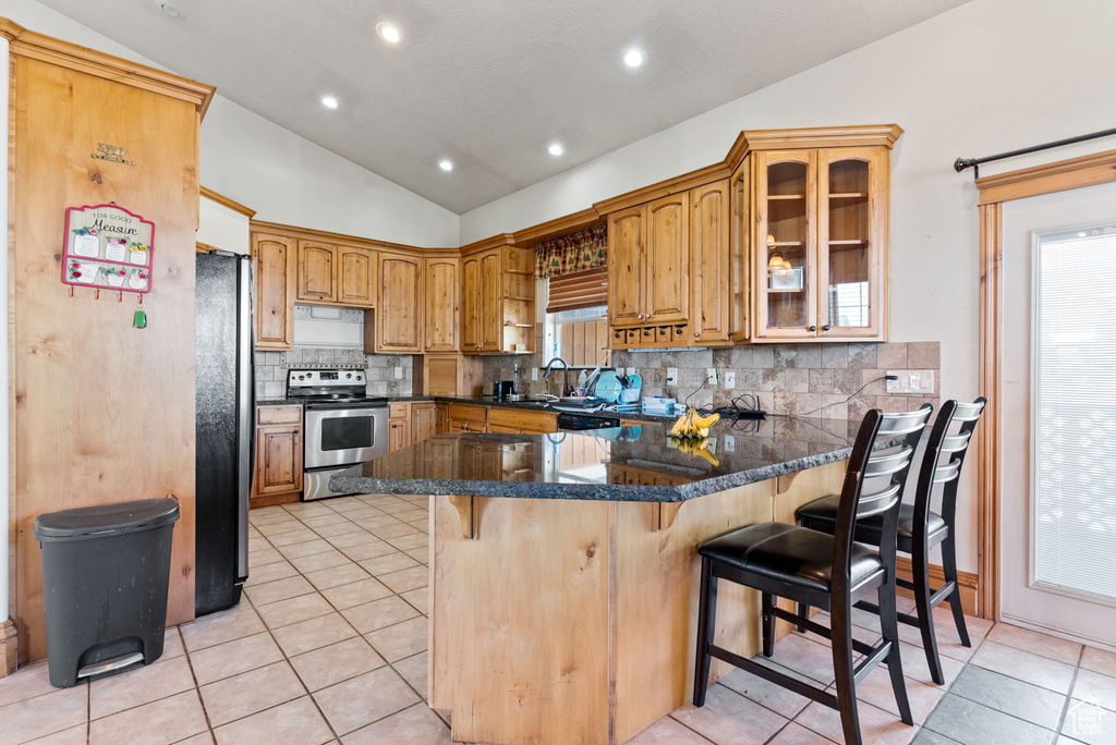 Kitchen with a breakfast bar area, appliances with stainless steel finishes, kitchen peninsula, lofted ceiling, and dark stone counters