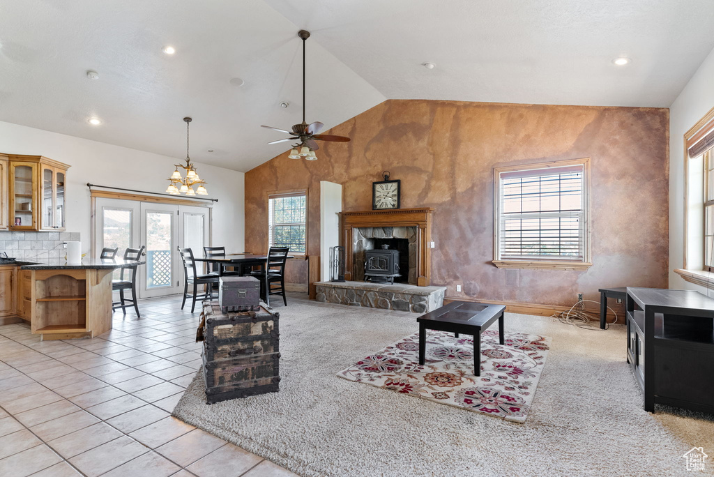 Living room with vaulted ceiling, ceiling fan with notable chandelier, light colored carpet, a wood stove, and a stone fireplace