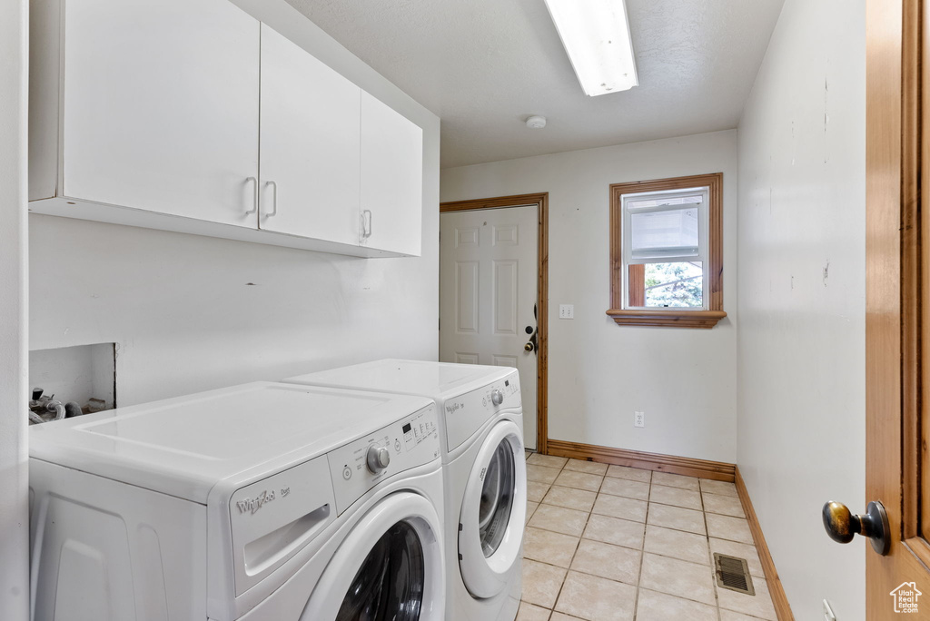 Clothes washing area with light tile patterned floors, cabinets, and washing machine and dryer