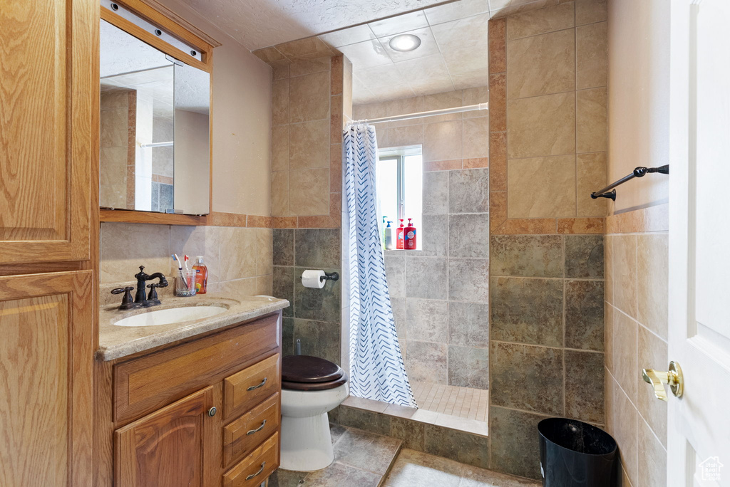 Bathroom featuring a shower with shower curtain, vanity, tile walls, toilet, and tile patterned floors