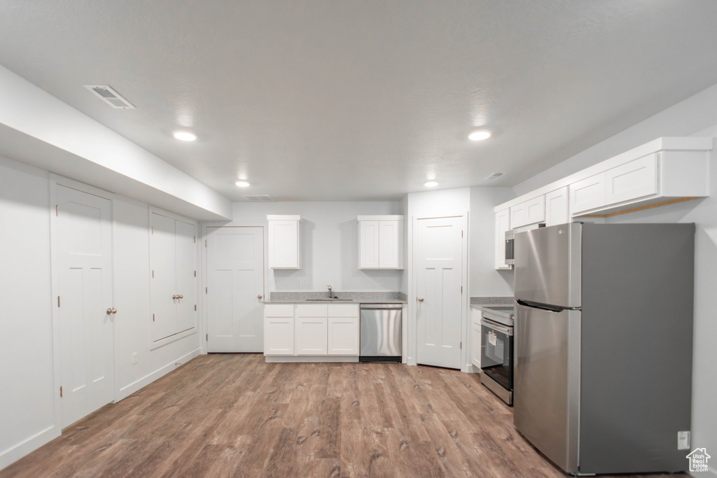 Kitchen with stainless steel appliances, sink, white cabinetry, and light hardwood / wood-style flooring