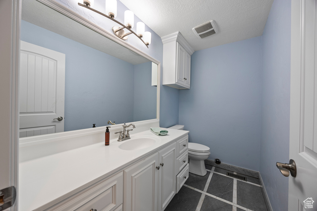 Bathroom featuring a textured ceiling, vanity, toilet, and tile patterned floors