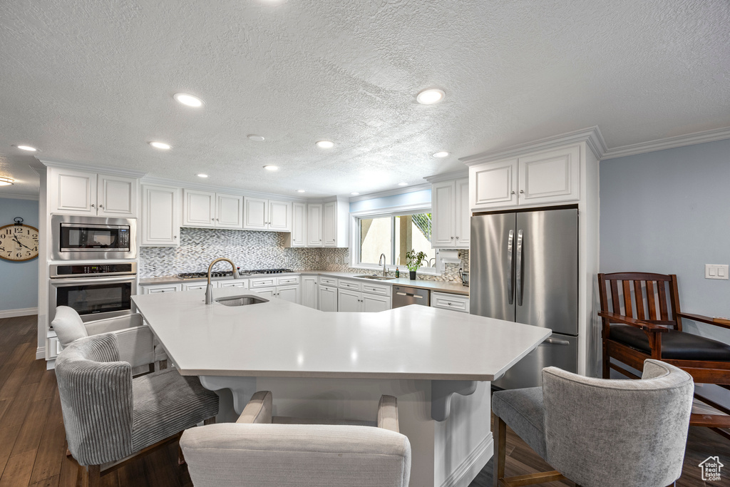 Kitchen with a breakfast bar area, dark hardwood / wood-style floors, appliances with stainless steel finishes, an island with sink, and sink