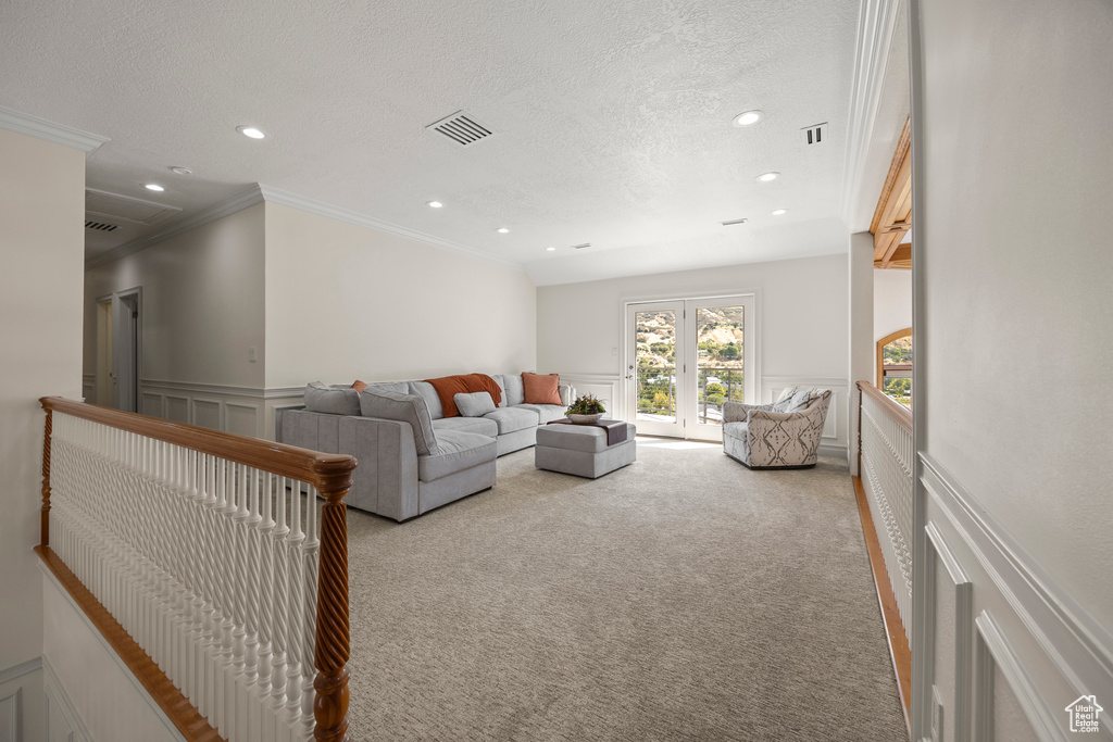 Carpeted living room featuring a textured ceiling, crown molding, and french doors