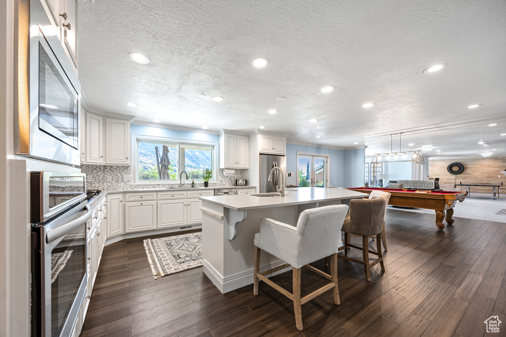 Kitchen featuring dark wood-type flooring, an island with sink, pool table, and a breakfast bar