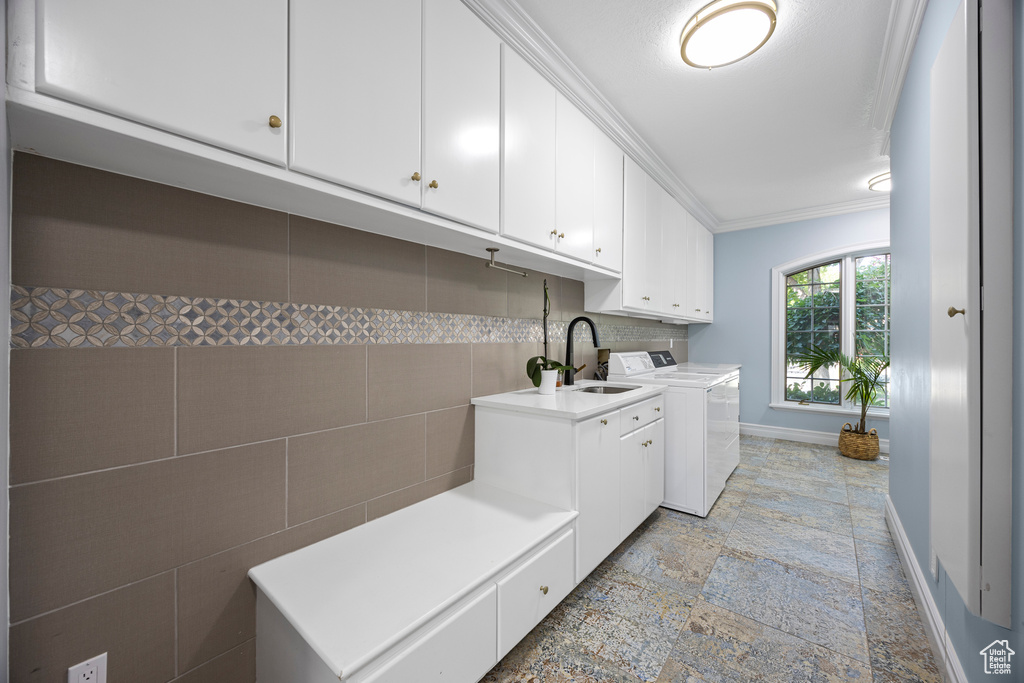 Washroom featuring cabinets, tile walls, ornamental molding, sink, and washing machine and dryer