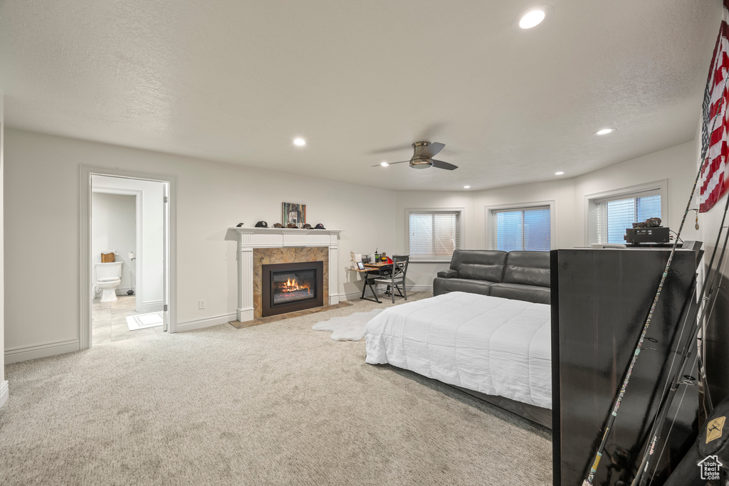 Bedroom with multiple windows, ceiling fan, a tile fireplace, and light carpet