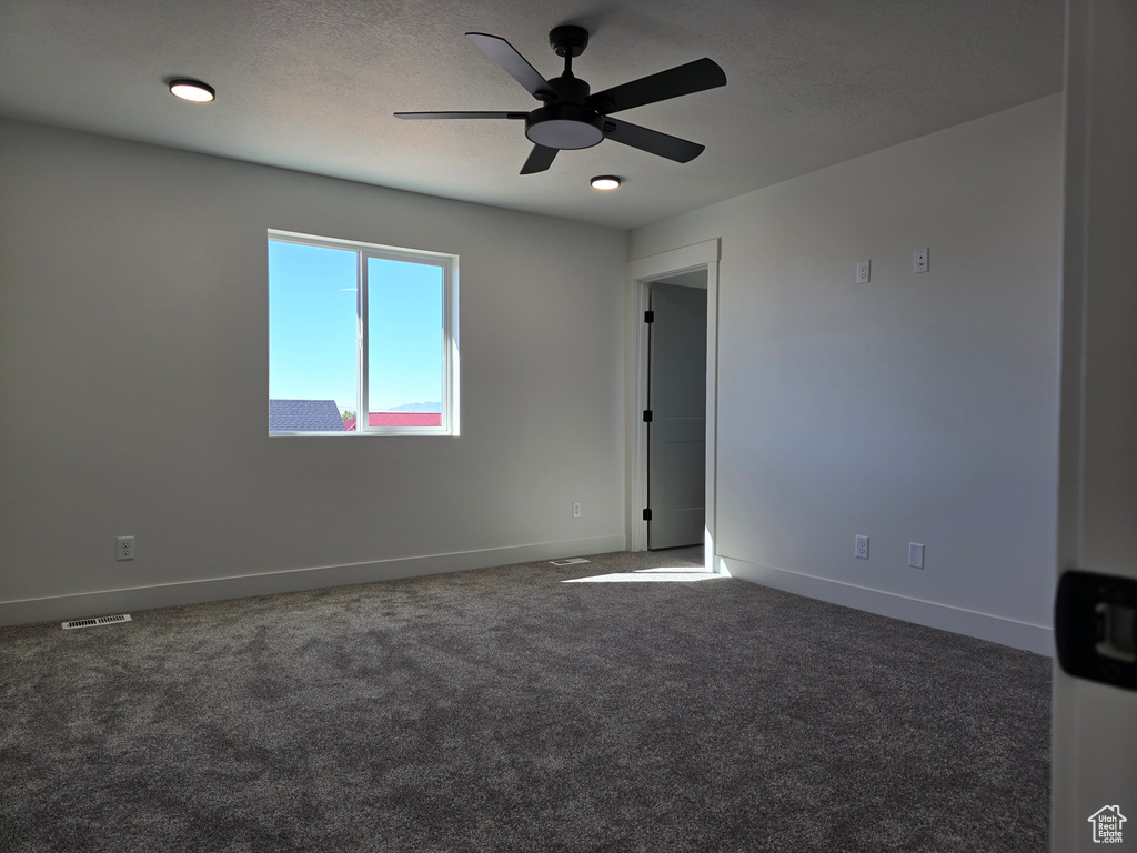 Empty room with ceiling fan and dark carpet