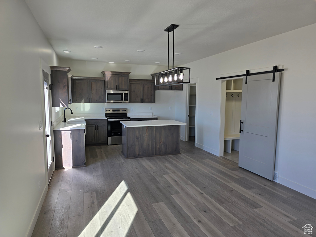 Kitchen with hanging light fixtures, a kitchen island, appliances with stainless steel finishes, dark hardwood / wood-style flooring, and a barn door