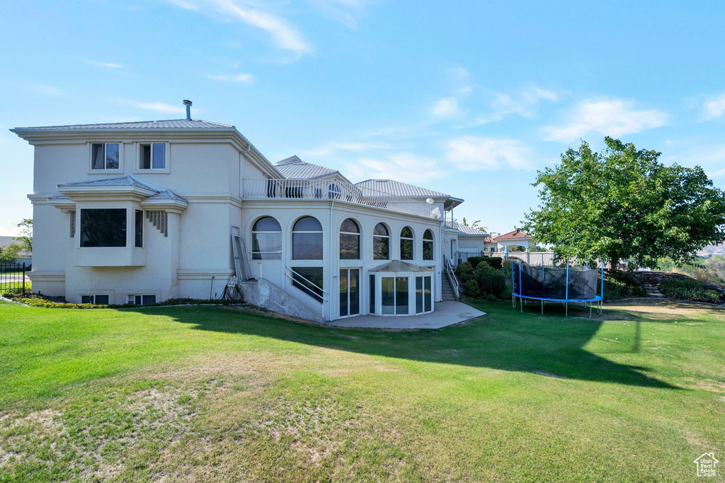 Back of house with a lawn and a trampoline