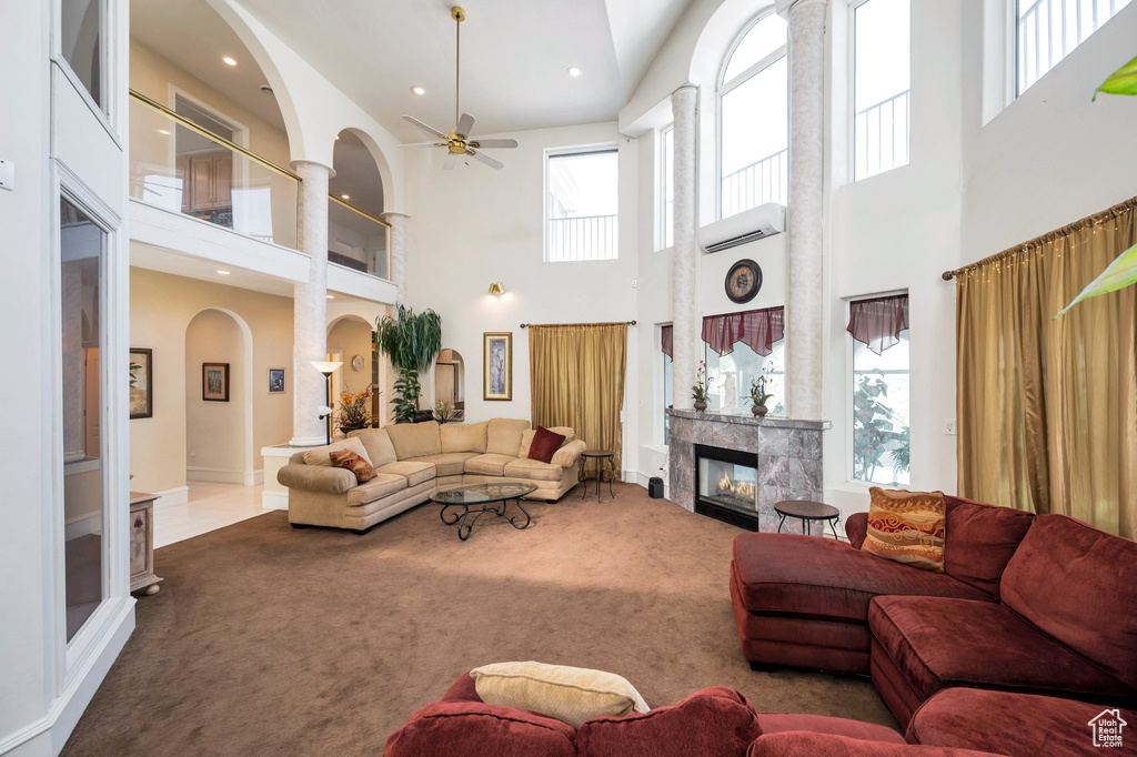 Carpeted living room with ceiling fan, a wall mounted air conditioner, a high end fireplace, and a towering ceiling