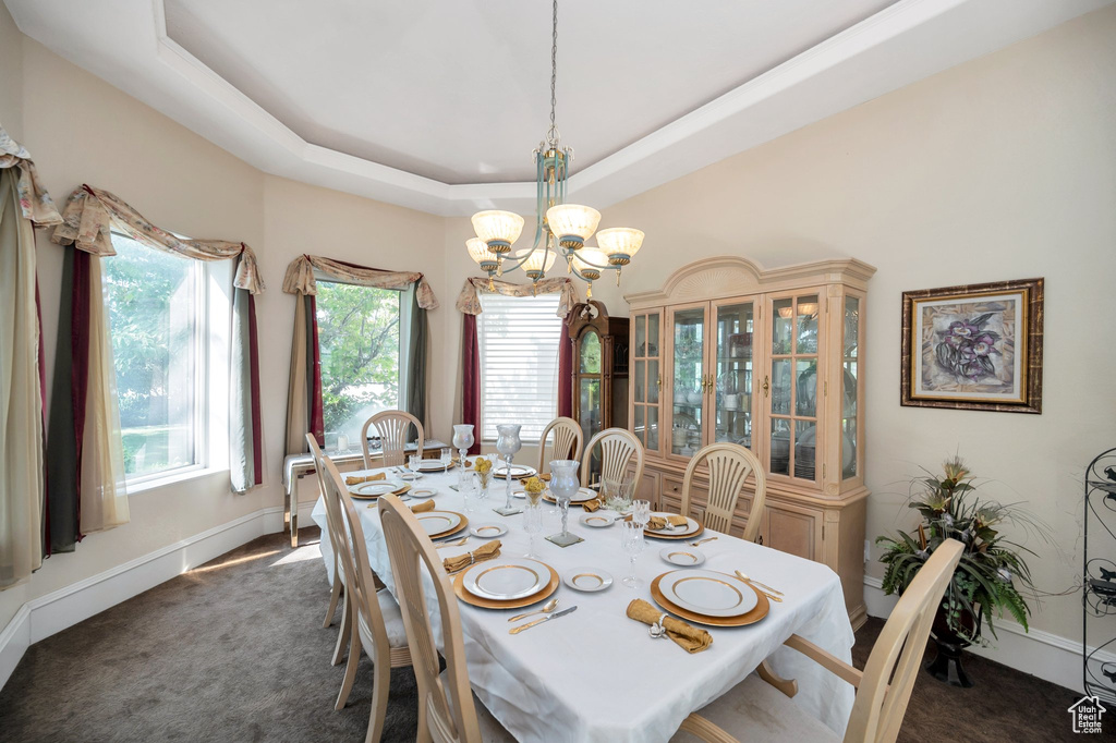 Dining room featuring dark carpet, a raised ceiling, and a notable chandelier