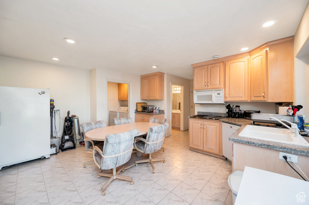 Kitchen with white appliances, light brown cabinets, sink, and washing machine and dryer