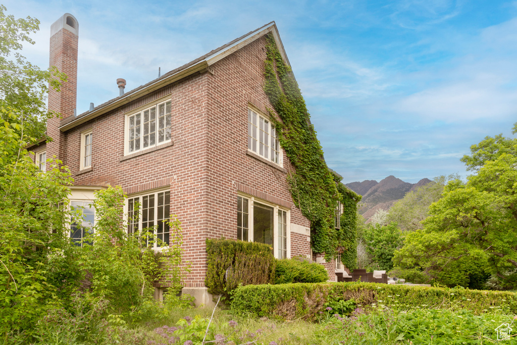 View of side of home featuring brick siding, a chimney, and a mountain view