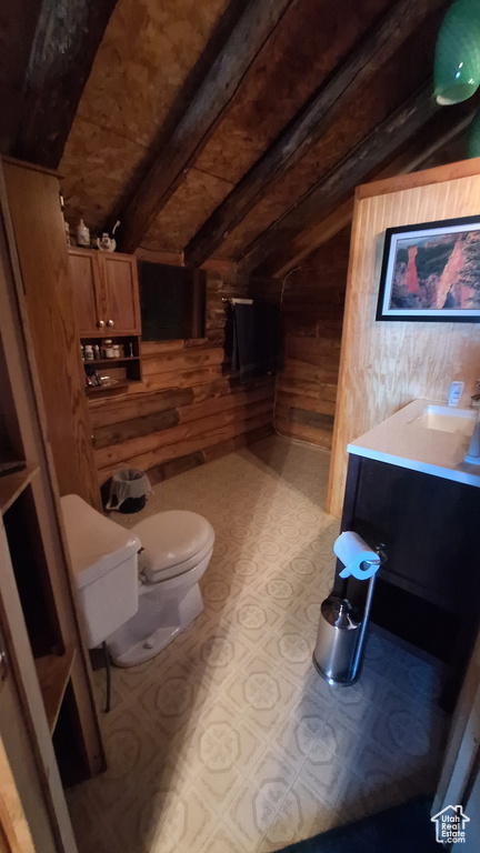 Bathroom with lofted ceiling with beams, toilet, wood walls, and vanity