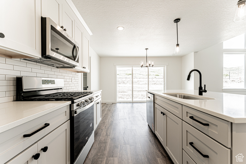 Kitchen with stainless steel appliances, a sink, a chandelier, dark wood-style floors, and backsplash