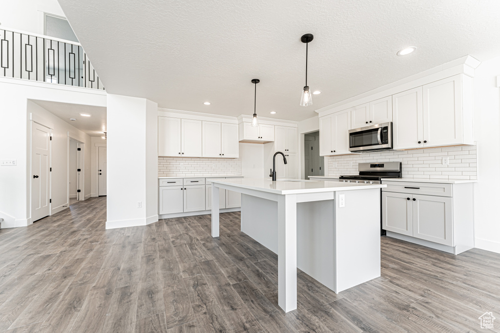 Kitchen with stainless steel appliances, light countertops, light wood-type flooring, backsplash, and an island with sink