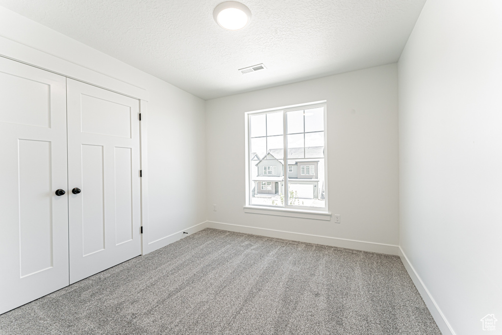 Unfurnished bedroom featuring carpet floors, baseboards, a textured ceiling, and a closet