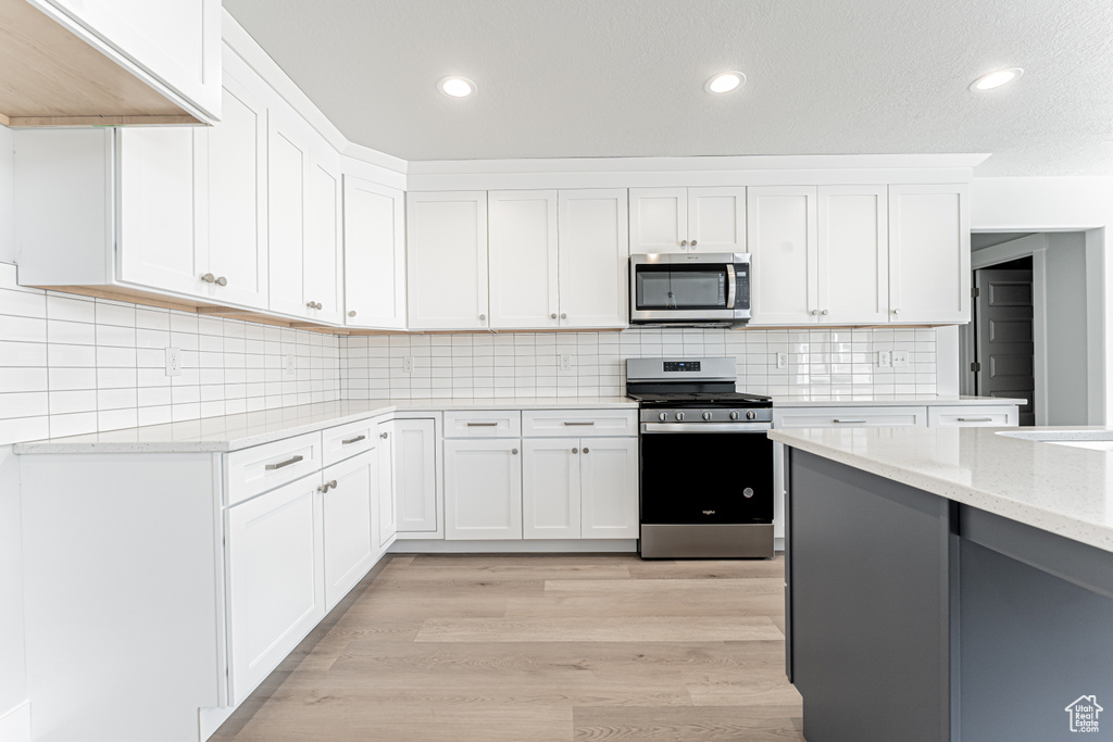 Kitchen with appliances with stainless steel finishes, white cabinets, light stone counters, recessed lighting, and tasteful backsplash