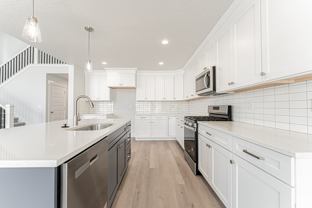 Kitchen with stainless steel appliances, a sink, light wood finished floors, white cabinets, and recessed lighting