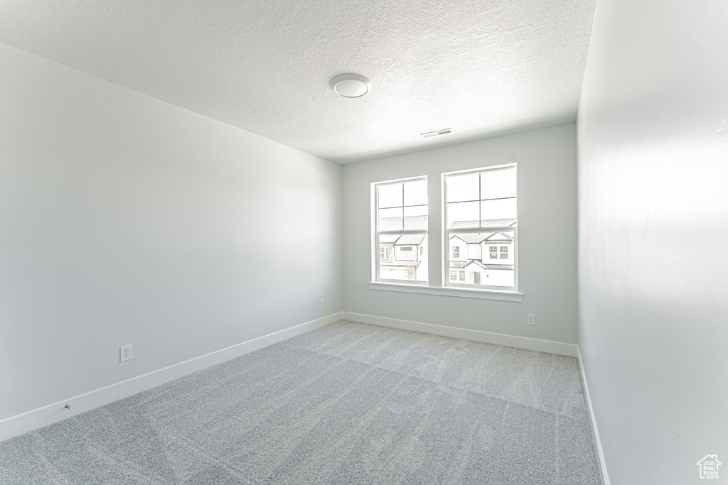 Spare room with light carpet, baseboards, and a textured ceiling