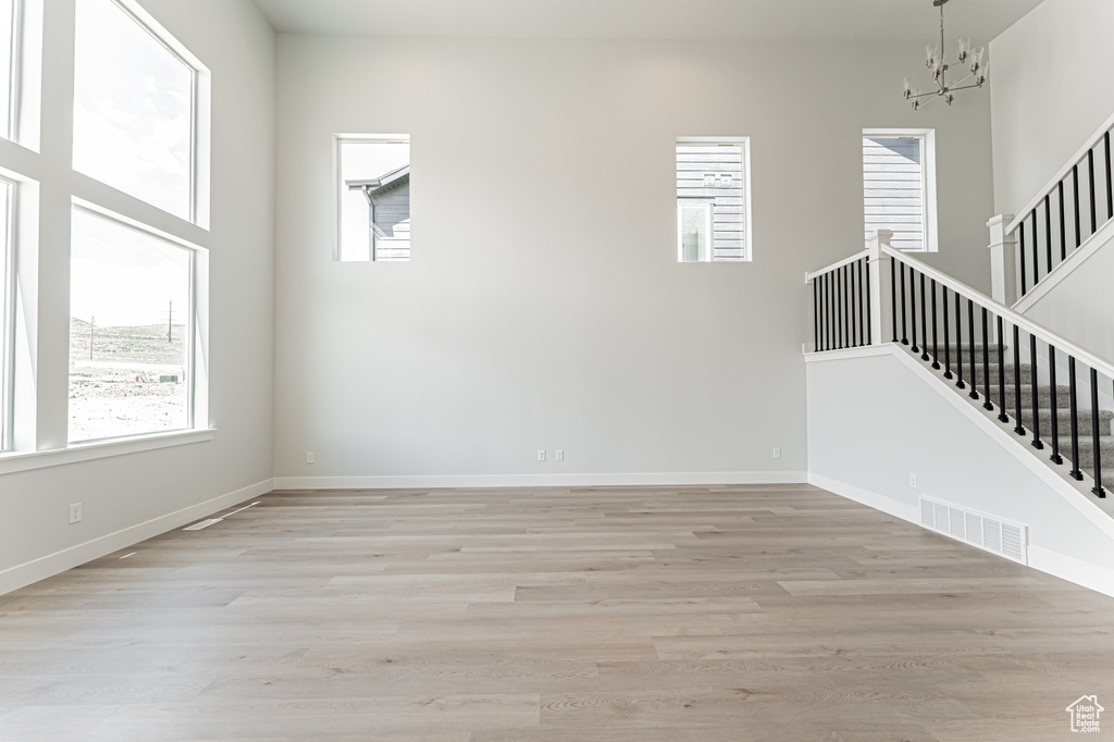 Unfurnished living room with healthy amount of natural light, a chandelier, and stairway