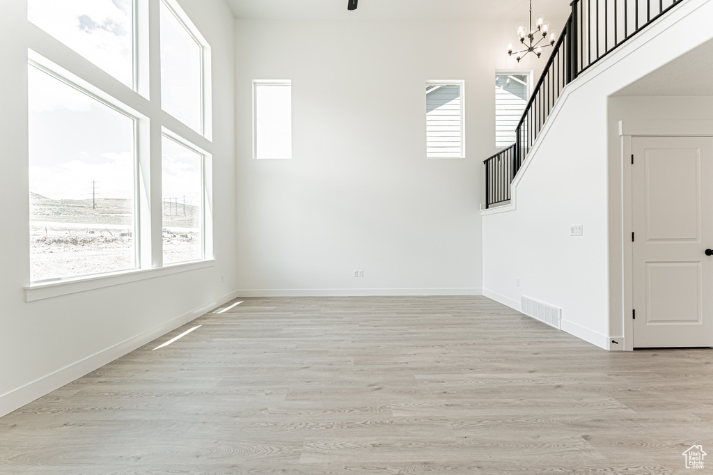 Empty room featuring a chandelier, light wood-type flooring, baseboards, and a high ceiling