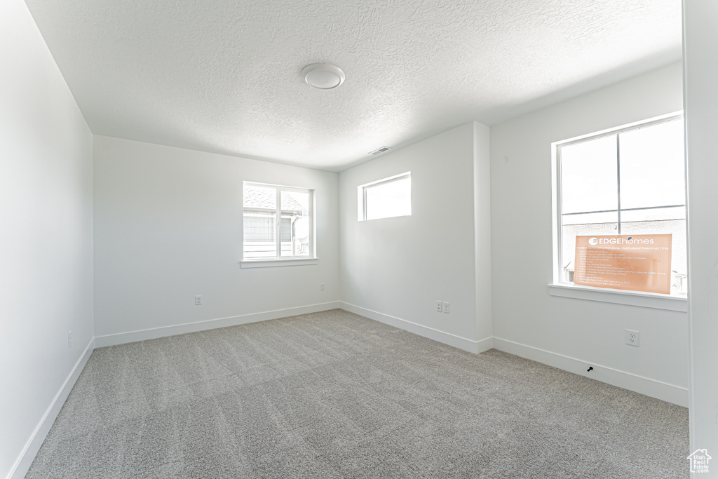 Carpeted spare room featuring a textured ceiling and baseboards