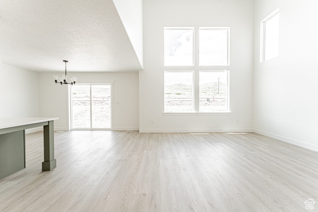 Unfurnished living room with a chandelier, light wood-style floors, baseboards, and a textured ceiling