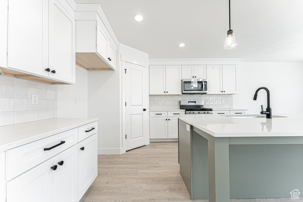 Kitchen with appliances with stainless steel finishes, a sink, tasteful backsplash, light wood-style flooring, and recessed lighting