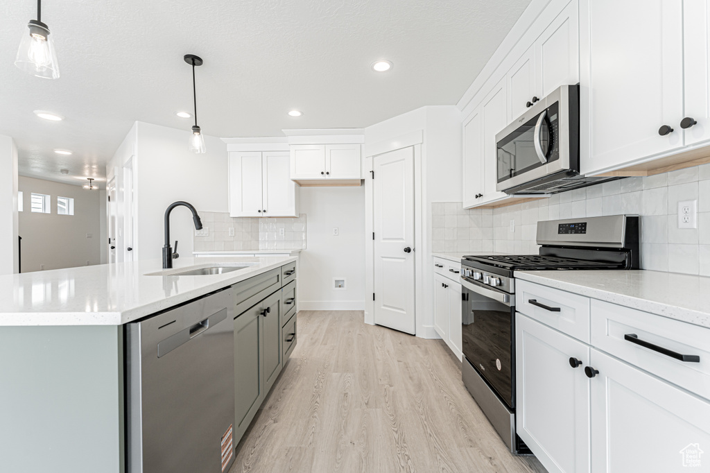 Kitchen featuring appliances with stainless steel finishes, a sink, light wood finished floors, white cabinetry, and tasteful backsplash