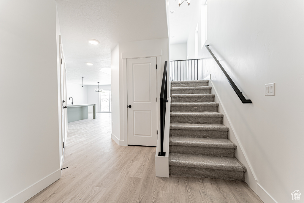 Stairs with wood finished floors, baseboards, and a chandelier