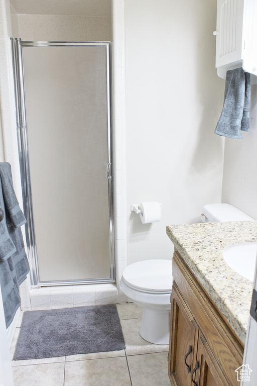 Bathroom featuring a shower with door, vanity, toilet, and tile patterned flooring