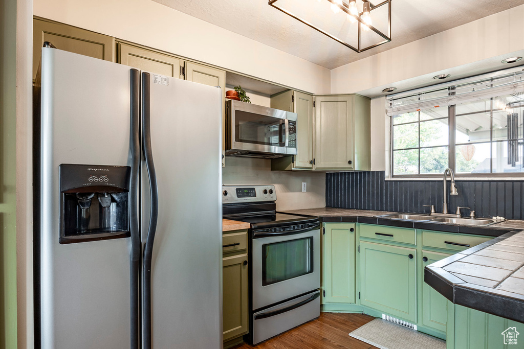 Kitchen featuring hardwood / wood-style floors, tile countertops, appliances with stainless steel finishes, sink, and green cabinetry