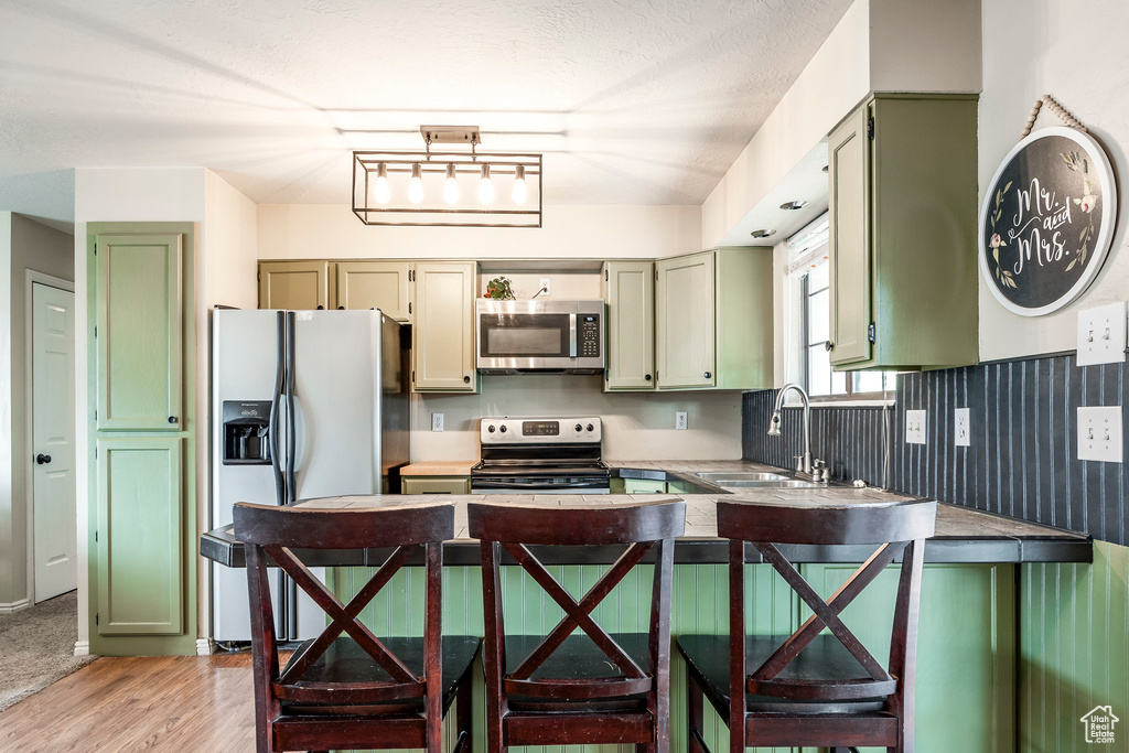 Kitchen with a kitchen bar, stainless steel appliances, kitchen peninsula, sink, and light hardwood / wood-style floors