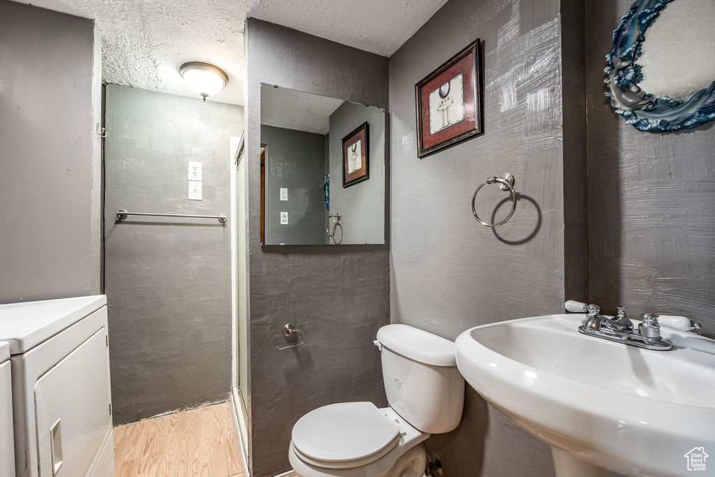 Bathroom with hardwood / wood-style floors, toilet, sink, washer / dryer, and a textured ceiling